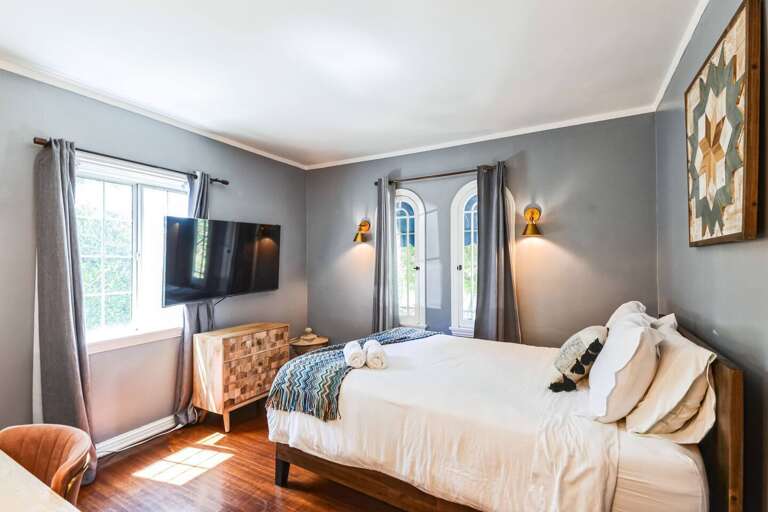 Relax in our queen bedroom featuring a large wall-mounted TV, perfect for unwinding with your favorite shows and movies.  Relax in our queen bedroom featuring a large wall-mounted TV, perfect for unwinding with your favorite shows and movies.